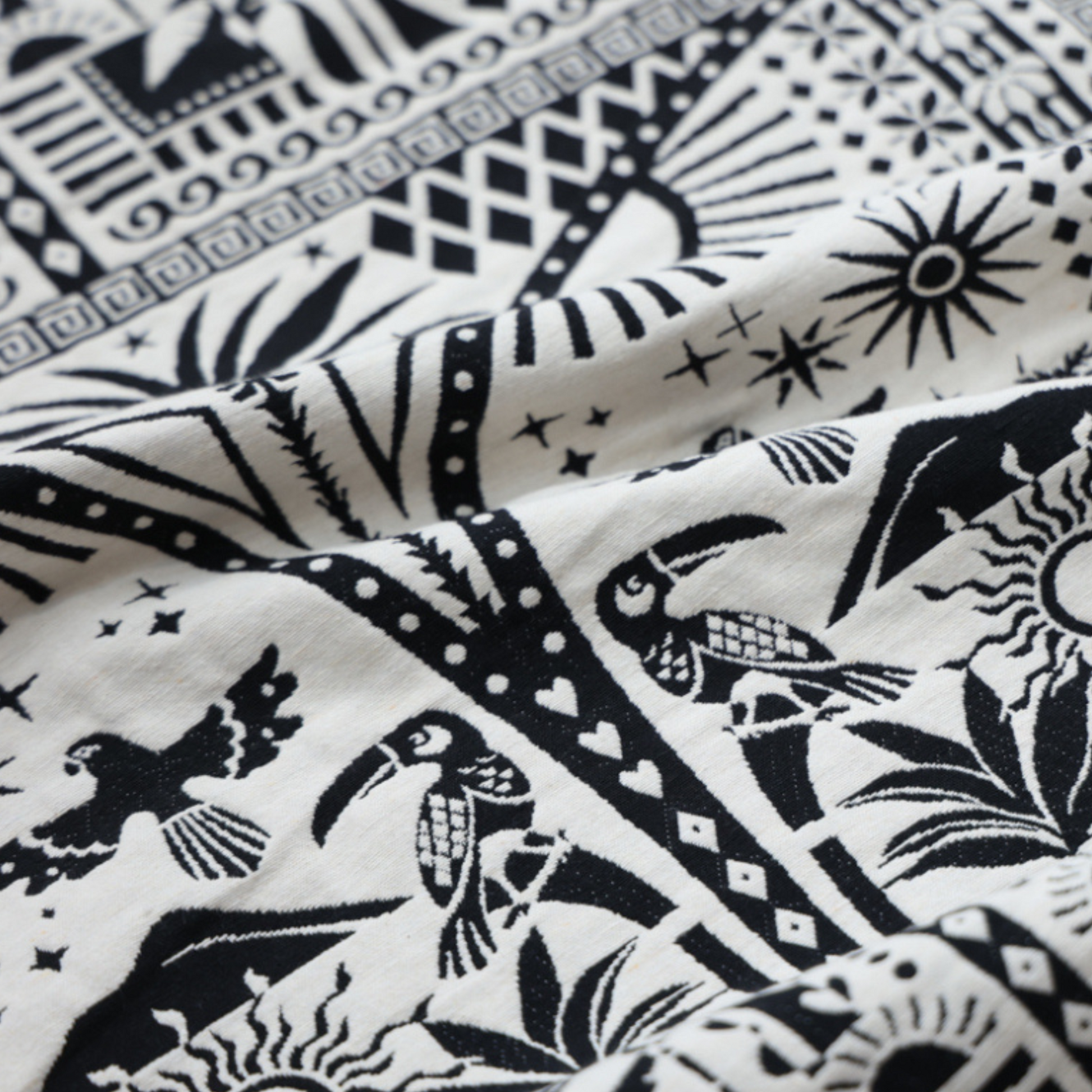 close up of black and white fabric. including geometric shapes, birds, and plants, with two front pockets that match the detailed print.