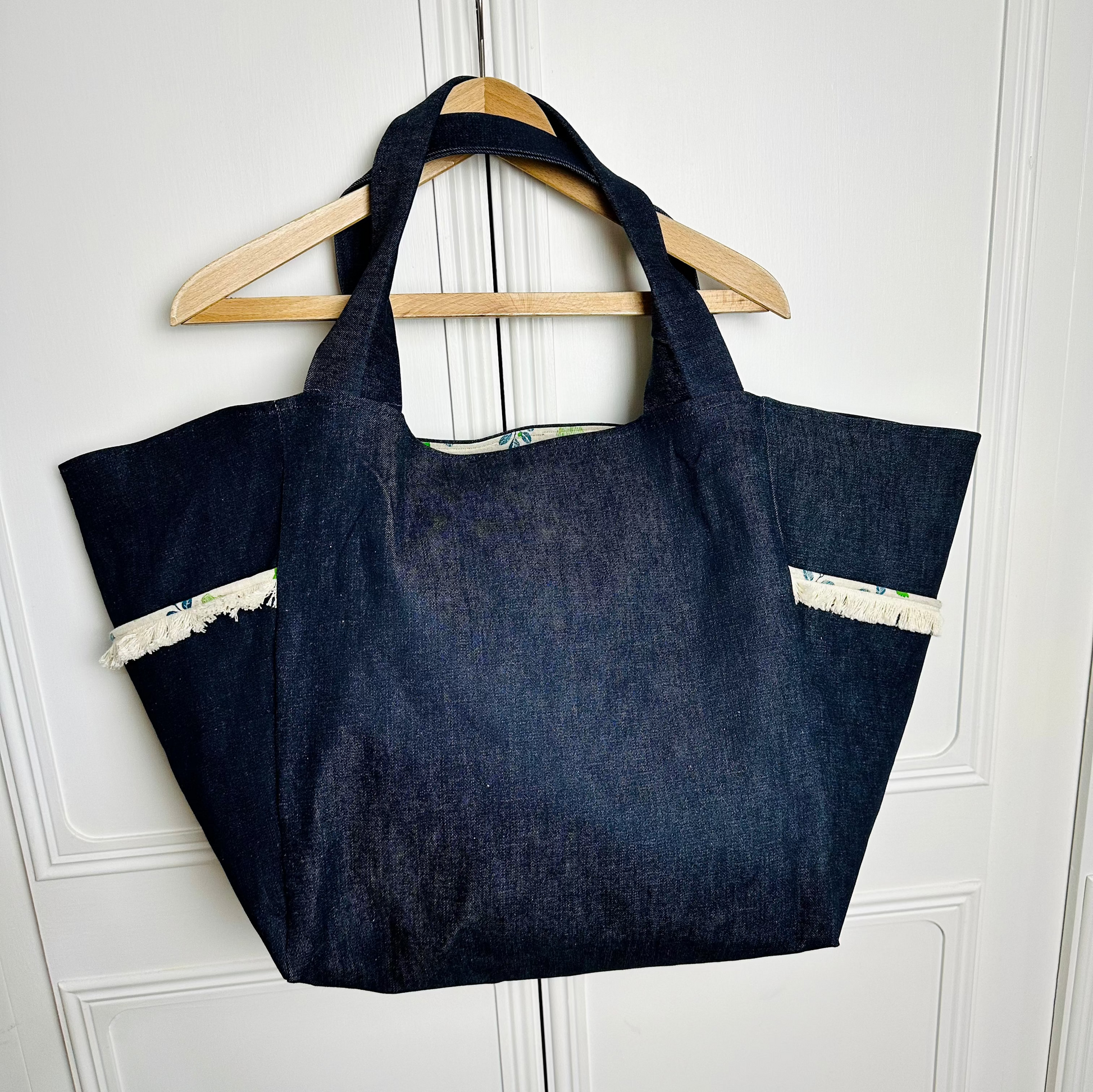 A dark blue denim bag hanging on a hanger against a white wall