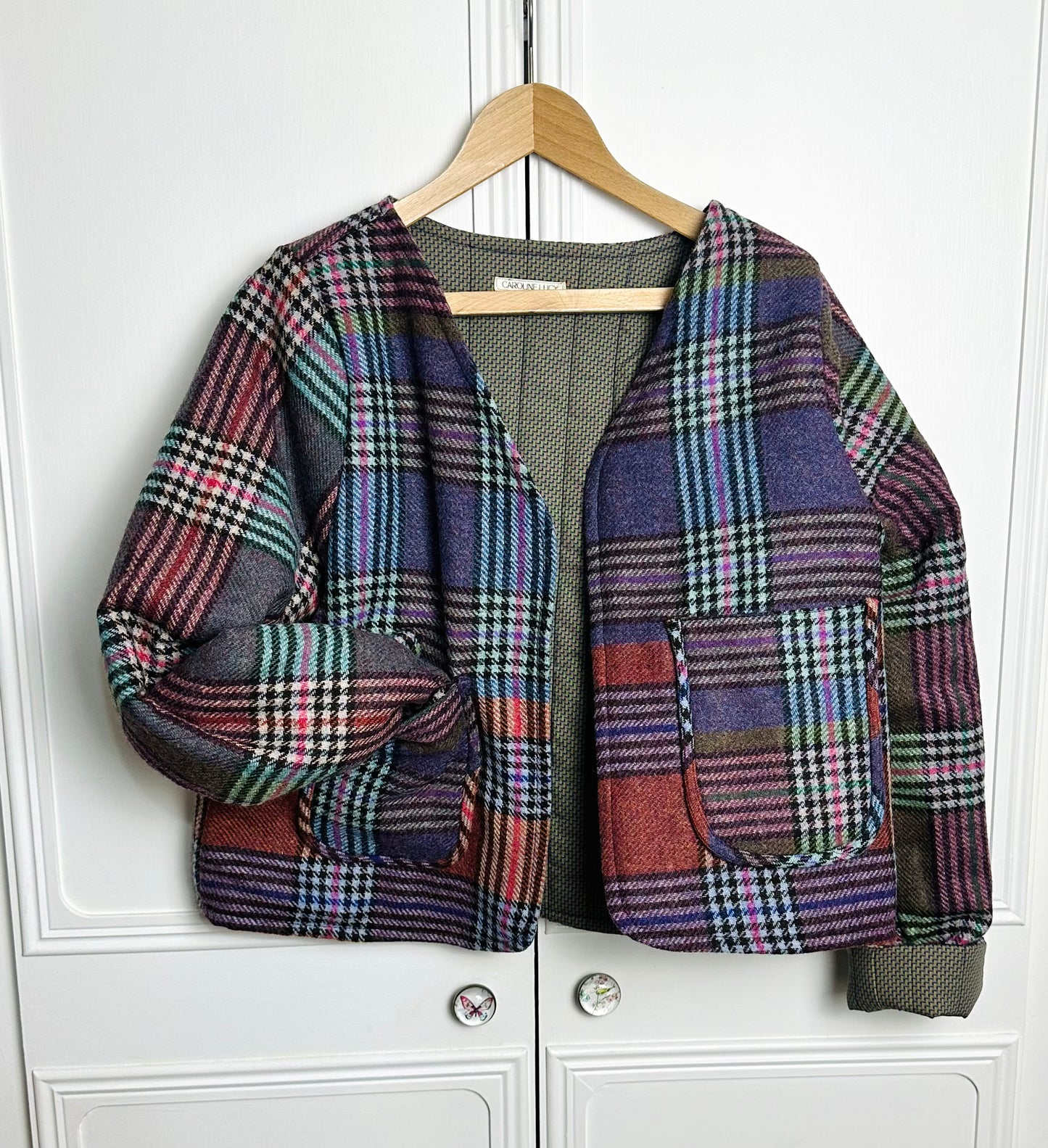 A cropped wool checked jacket in multi colours is hung on a hanger against a white background