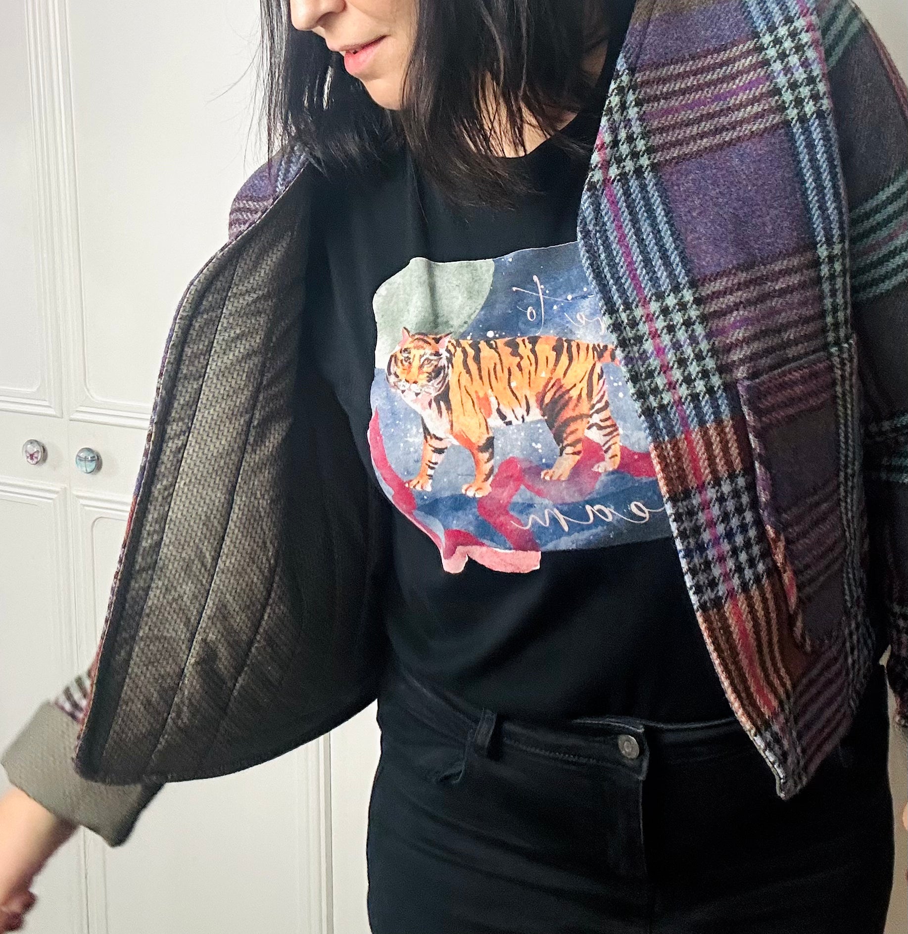 A woman standing against a white background is wearing a multicoloured checked cropped blazer. She is wearing black jeans.