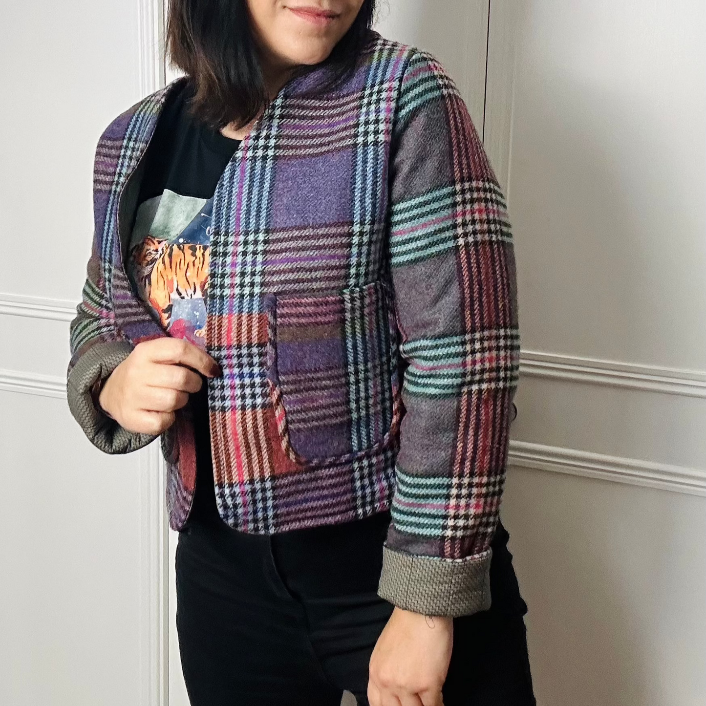 A woman standing against a white background is wearing a multicoloured checked cropped blazer. She is wearing black jeans.