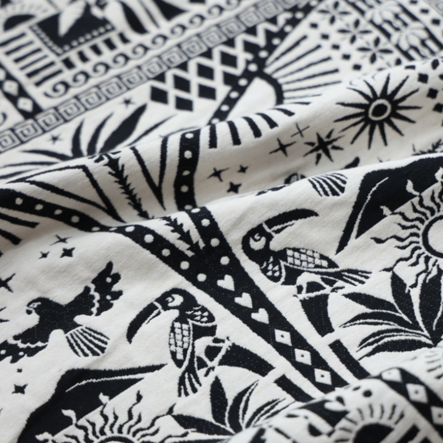 close up of black and white fabric. including geometric shapes, birds, and plants, with two front pockets that match the detailed print. 